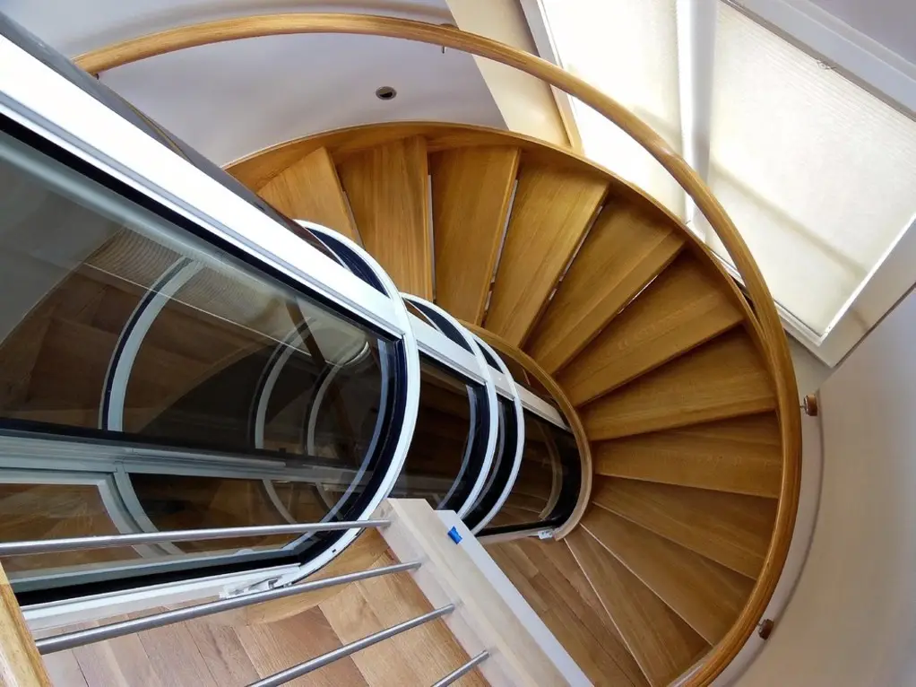 Pneumatic vacuum elevator installed beside a wooden spiral staircase