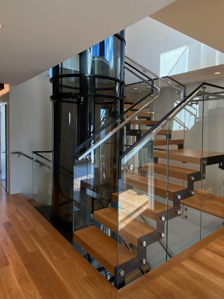 Glass cylindrical home elevator beside a modern staircase.
