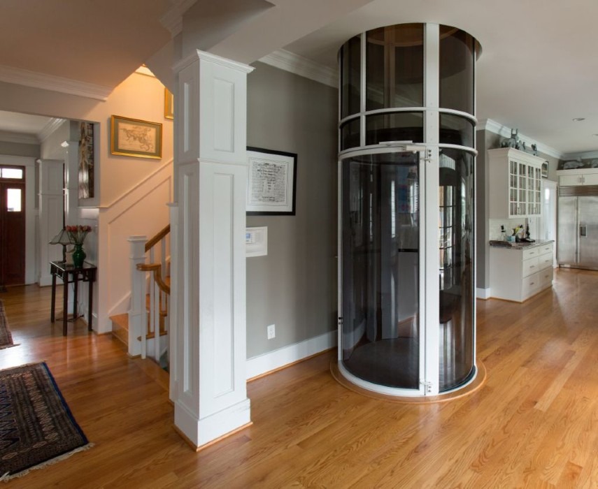 Residential interior featuring a cylindrical glass vacuum home elevator with a white and stainless-steel finish